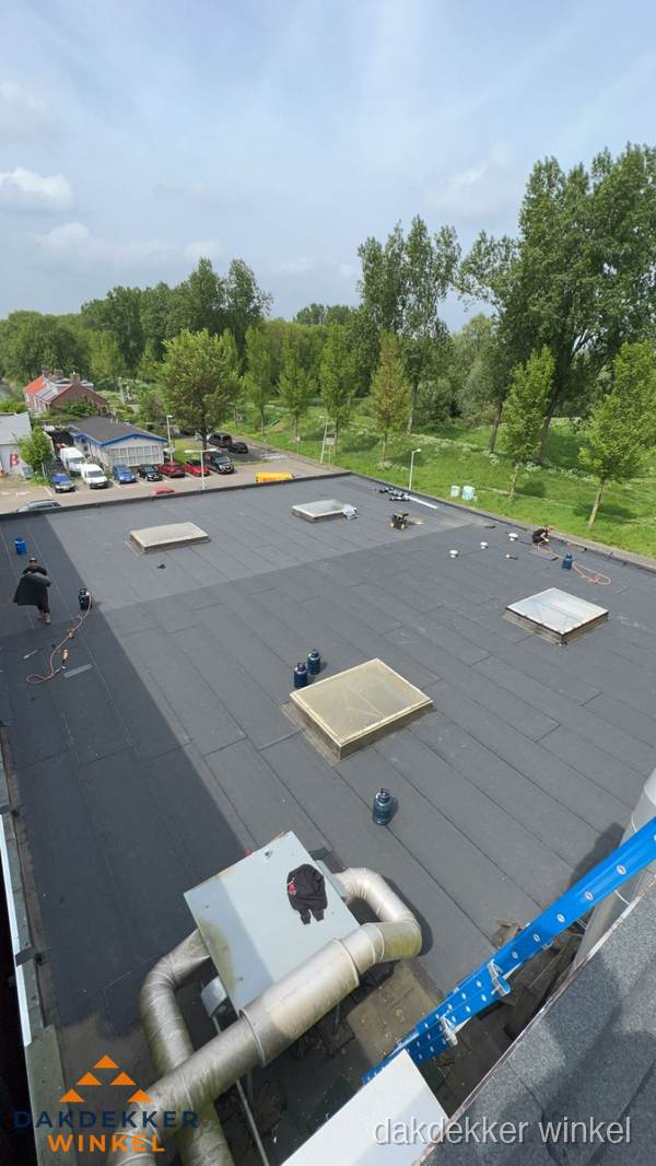 Dakdekker aan het werk op groot plat dak met bitumen in Winkel