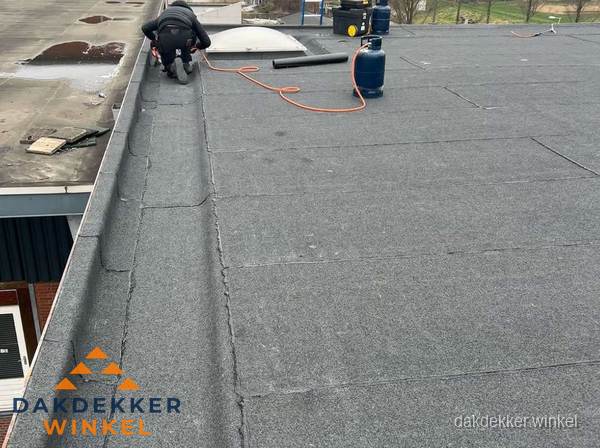 Dakdekker repareert bitumen dakbedekking op groot plat dak in Winkel